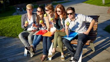 Jugendliche sitzen auf einer Bank und essen Äpfel