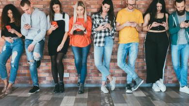 Junge Leute in einer Reihe, alle schauen auf Smartphones zu Artikel: Messenger Dienste - worauf Sie bei der Auswahl achten sollten