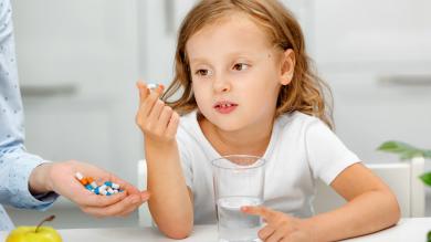 Kind vor Glas Wasser mit Tablette in Hand