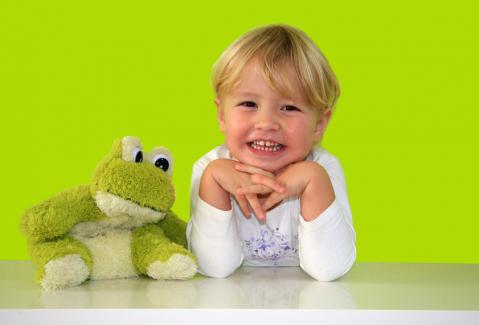 Kind mit Froschstofftier vor grünem Hintergrund.