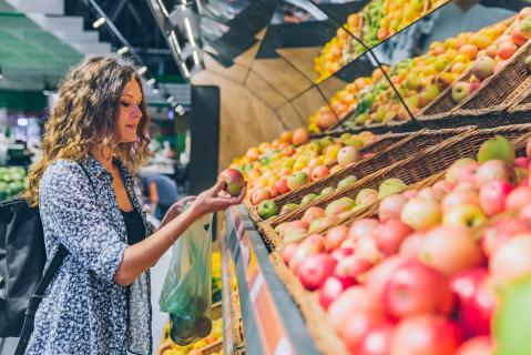Frau vor Regal mit Äpfeln im Supermarkt