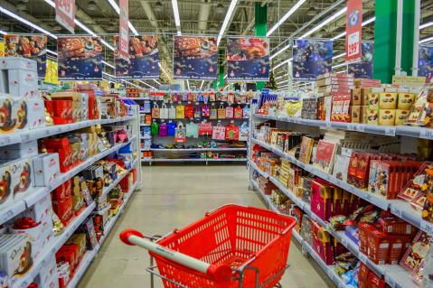 Einkaufswagen in rot steht leer zwischen den ganze Supermarktregalen gefüllt mit Weihnachtsschokolade