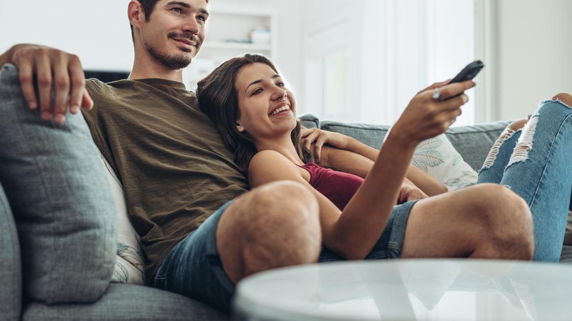 Paar kuschelt auf Sofa, Frau hat Fernbedienung in Hand