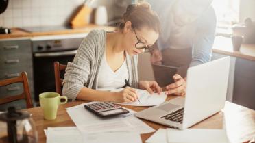 Frau an Tisch mit Laptop, Zetteln, Stift und Taschenrechner