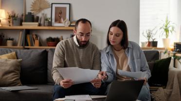 Mann und Frau sitzen auf auf Sofa mit Papieren in Hand