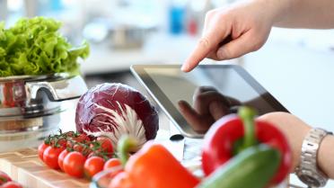 Nahaufnahme Hand zeigt auf Tablet, im Vordergrund verschiedenes Gemüse