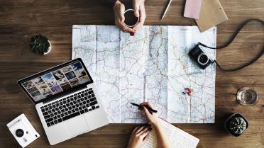 Reiseplanung mit Laptop und Landkarte an Tisch