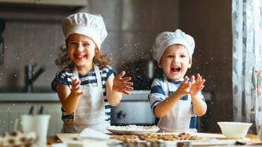 Zwei Kinder werfen Mehl in der Küche durch die Luft und backen