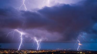Auf dem Foto sind mehre Blitze zu sehen, am unteren Bildrand Häuser. Der Himmel ist dunkel.