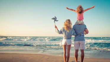 Familie am Strand von hinten, Kind auf Schultern des Vaters. Es ist Sommer.