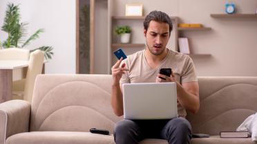 Mann erschrocken mit Kreditkarte vorm Rechner beim Onlineshopping