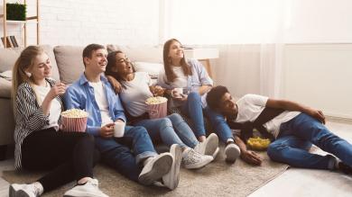 Junge Leute mit Popcorn sitzen auf dem Fußboden - Rundfunkbeitrag