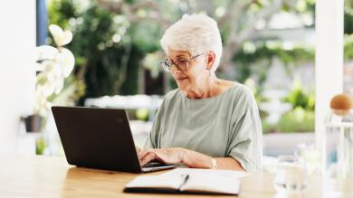 Frau mit weißem Haar sitzt vor Laptop