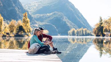 Pärchen auf Steg, See und Bergpanorama im Hintergrund zu Artikel: Grenznaher Urlaub: Wenn das Handy sich ins falsche Netz einwählt