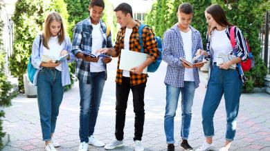 Mehrere junge Erwachsen stehen auf Weg nebeneinander, schauen in Bücher und Hefte zu Artikel: Gut versichert zum Berufsstart 