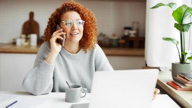 Frau mit Telefon am Ohr vor Laptop an Küchentisch