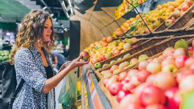 Frau vor Regal mit Äpfeln im Supermarkt