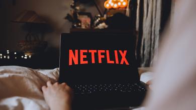 Person sitzt auf Sofa mit Laptop. Auf Bildschirm steht Netflix