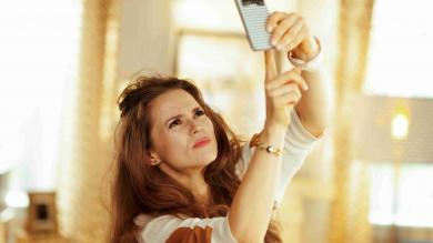 Frau hebt Handy in die Höhe in ihrere Wohnung für besseren Empfang