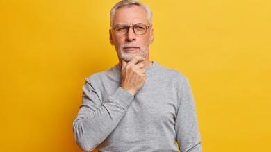 Ältererer Mann auf gelbem Hintergrund hat Hand am Kinn und schaut nachdenklich