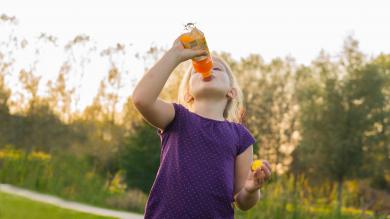 Kind trinkt draußen ein Kindergetränk, ähnlich Multivitaminsaft aus einer Flasche