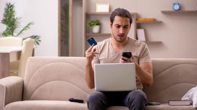 Mann erschrocken mit Kreditkarte vorm Rechner beim Onlineshopping