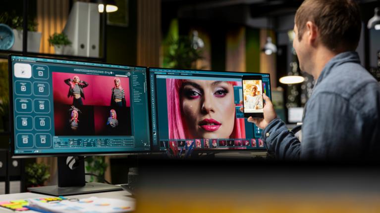 Bildbearbeiter sitzt vor zwei Monitoren und bearbeitet ein Bild