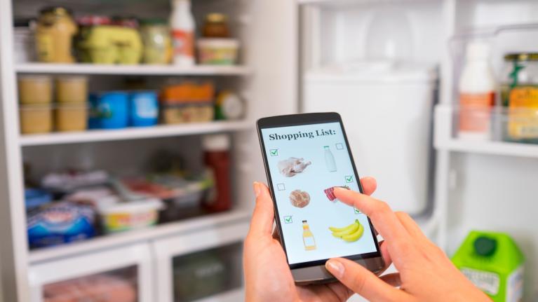 Digitale Einkaufsliste erstellen vor geöffnetem Kühlschrank