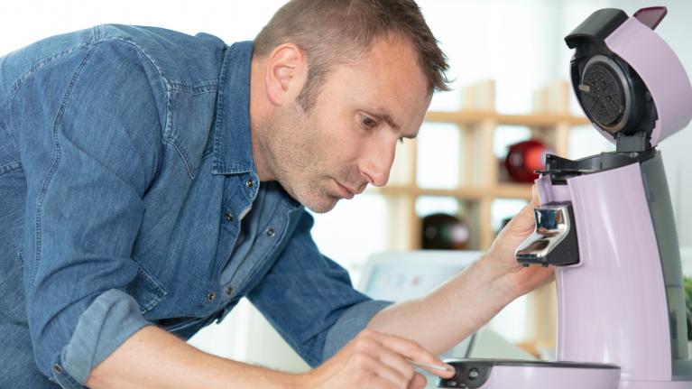 Mann drückt Knopf auf kaputter Kaffeemaschine