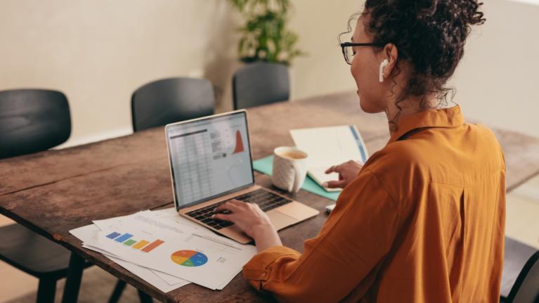 Frau schräg von hinten sitzt vor Laptop