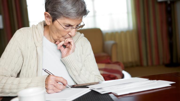 Ältere Frau an Tisch mit Papieren und Stift