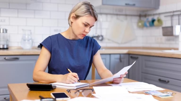 Frau sitzt an Küchentisch mit Papieren, Stift und Zettel