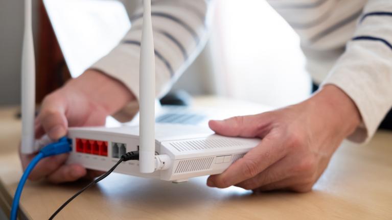 Mensch steckt Kabel in Glasfasermodem