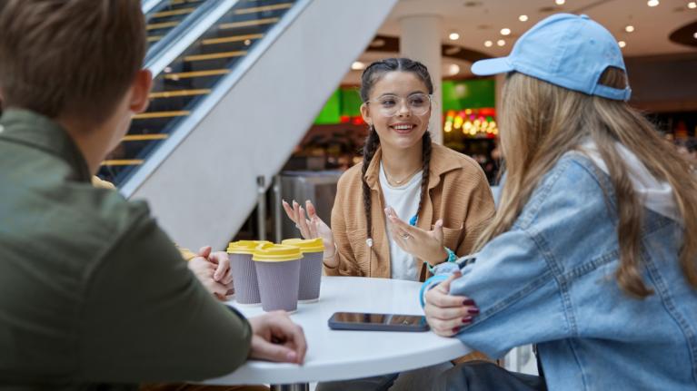 Jugendliche sitzen in Einkaufszentrum mit Kaffeebechern