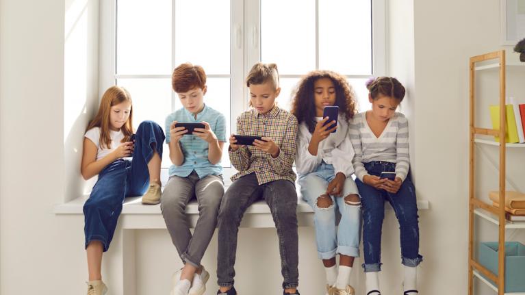 Kinder auf Fensterbank sitzend mit Smartphones, In-App-Käufe
