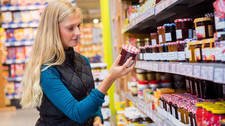 Junge Frau hält Marmeladenglas im Supermarkt in der Hand, betrachtet das Etikett