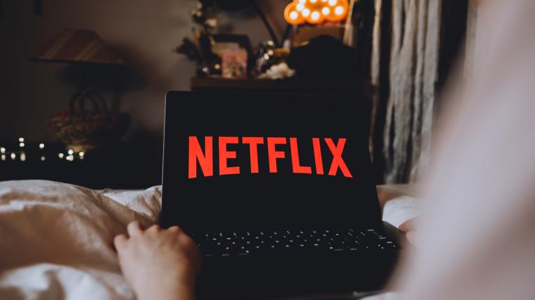 Person sitzt auf Sofa mit Laptop. Auf Bildschirm steht Netflix