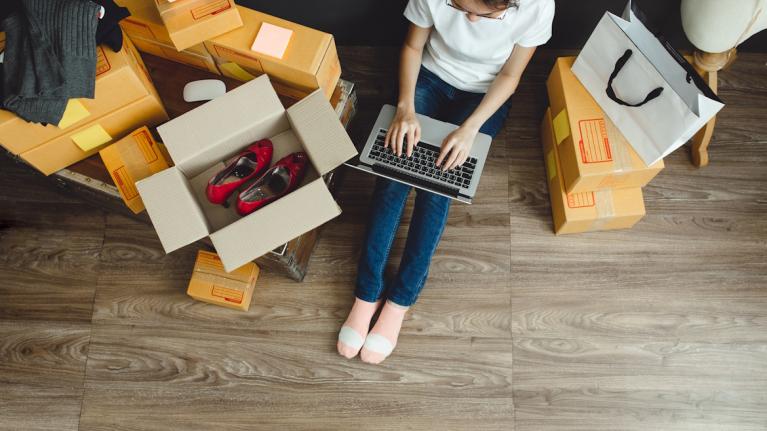 Frau mit Laptop und Kartons mit bestellten Produkten auf Boden China Shops