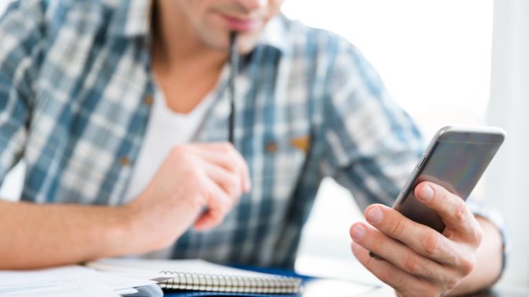 Mann mit Smartphone und Block zum Rechnen