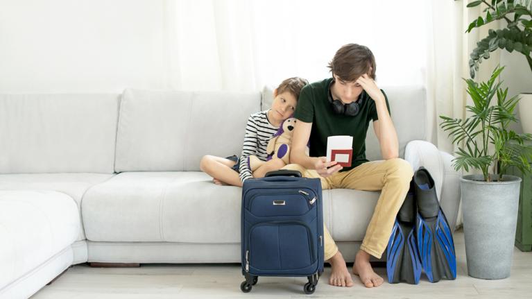 Zwei enttäuschte Jungs auf Sofa mit Koffer davor