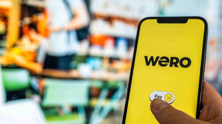 Wero Pay App auf Handy im Vordergrund - Hintergrund Supermarktregale verschwommen