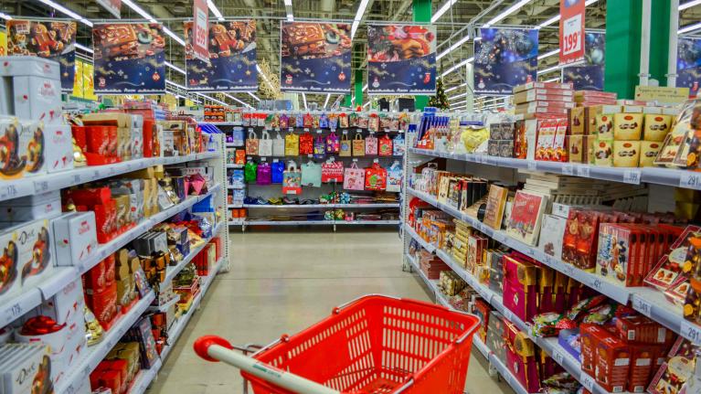 Einkaufswagen in rot steht leer zwischen den ganze Supermarktregalen gefüllt mit Weihnachtsschokolade