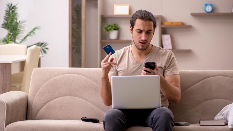Mann erschrocken mit Kreditkarte vorm Rechner beim Onlineshopping