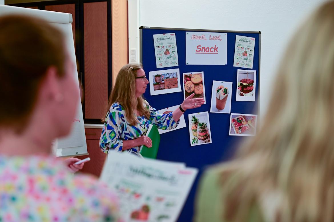 Frau erklärt etwas an Stellwand zu Trends bei Snacks und Getränken in Schule