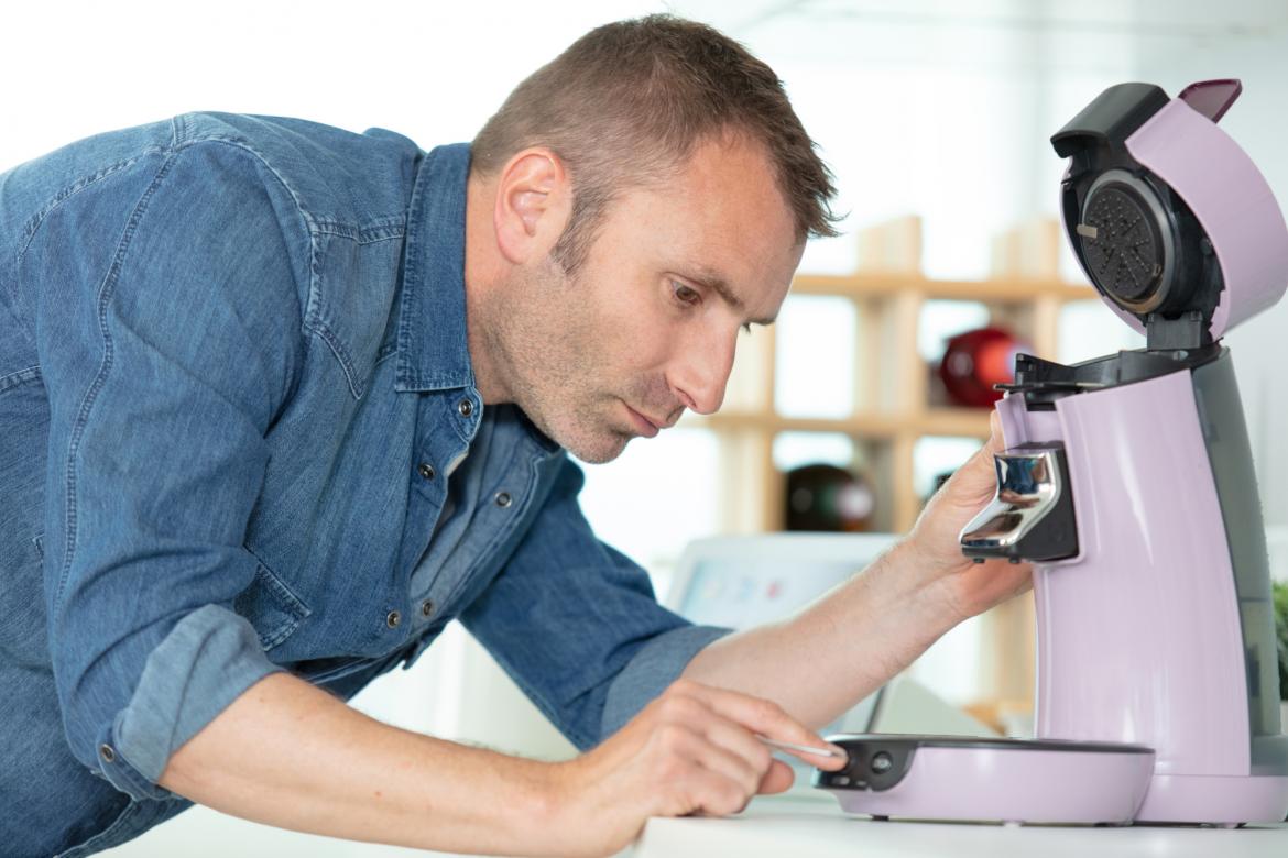 Mann drückt Knopf auf kaputter Kaffeemaschine