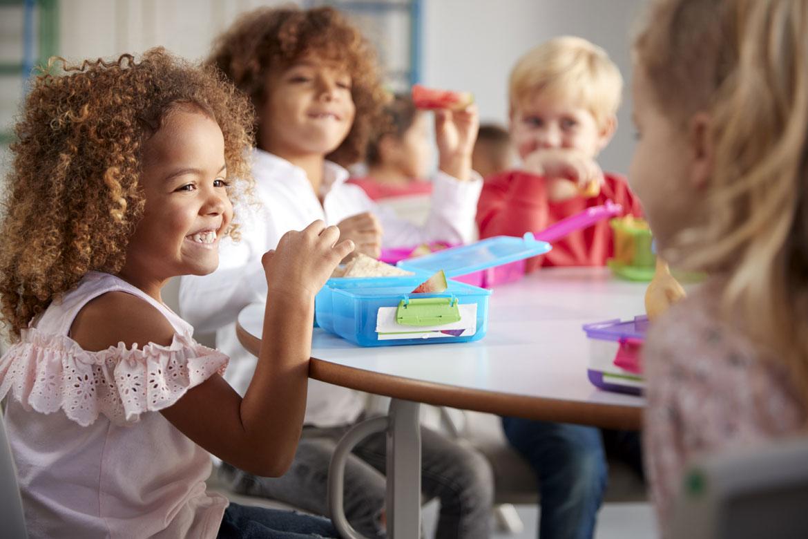 Mehrere Kinder sitzen mit Brotdosen am Tisch zu Artikel: Bunte Frühstücksbox-Ideen für die Kita