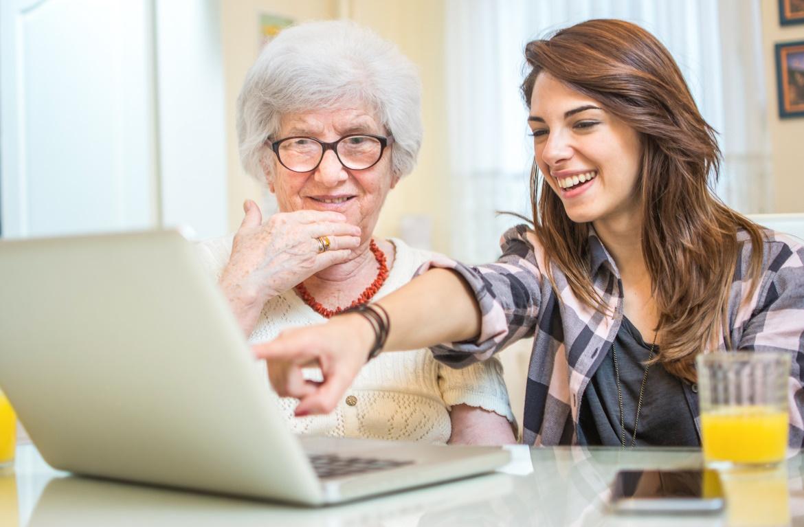 Junge Frau zeigt Seniorin etwas am Laptop zu digitale Vorsorge