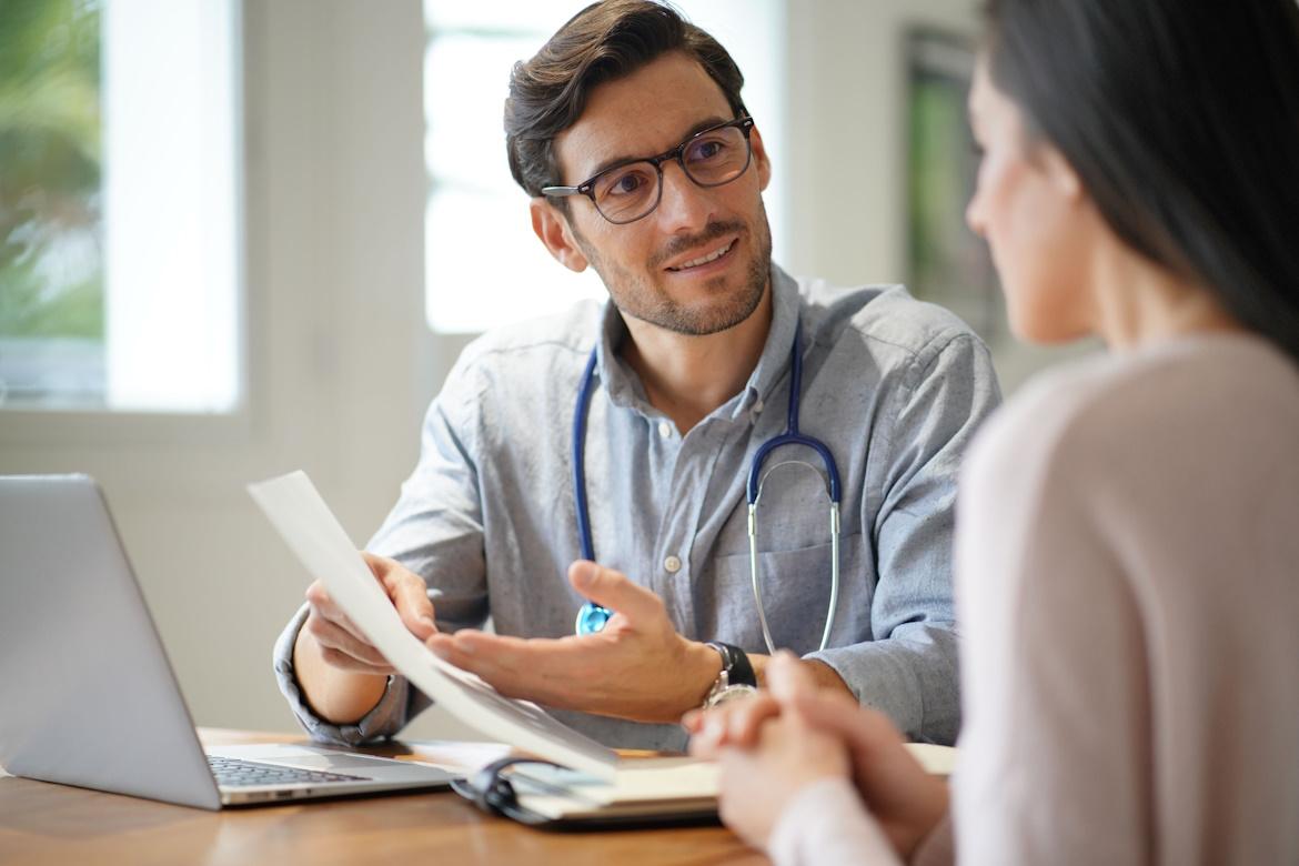 Arzt mit Dokument in Hand spricht mit Patientin zu Fokuswoche Vorsorge