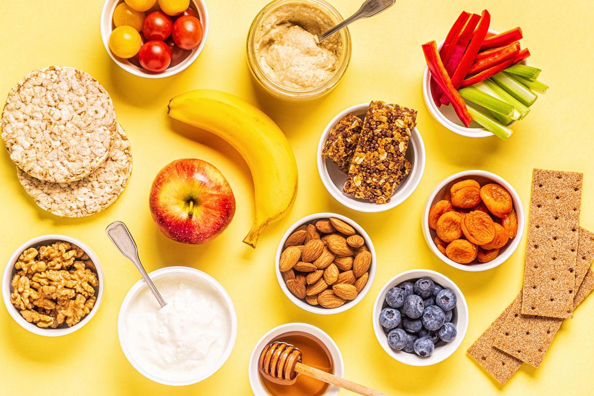Verschiedene Lebensmittel wie Banane, Gemüse Nüsse Obst in Schälchen auf Tisch zu Artikel: Gesunde Frühstücks- und Snackkultur für Kids