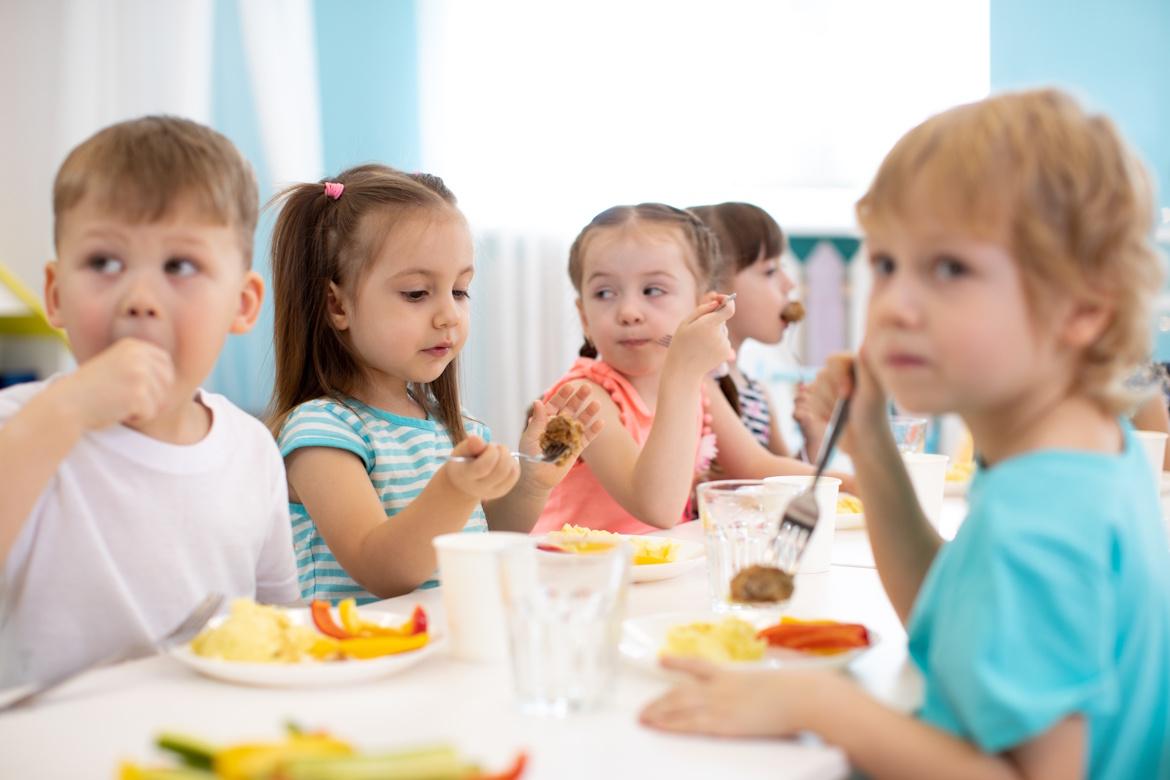 Kindergartenkinder essen an großem Tisch
